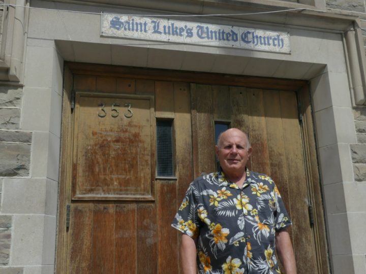 Jim Keenan, standing in a black and yellow Hawaiian shirt, in front of a labelled entrance to Saint Luke's United