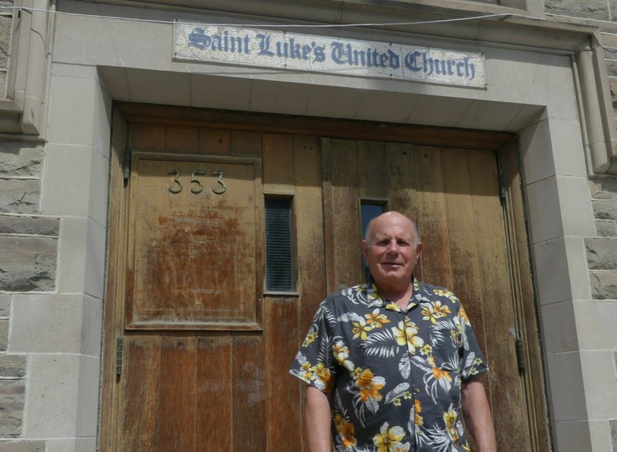 Jim Keenan, standing in a black and yellow Hawaiian shirt, in front of a labelled entrance to Saint Luke's United