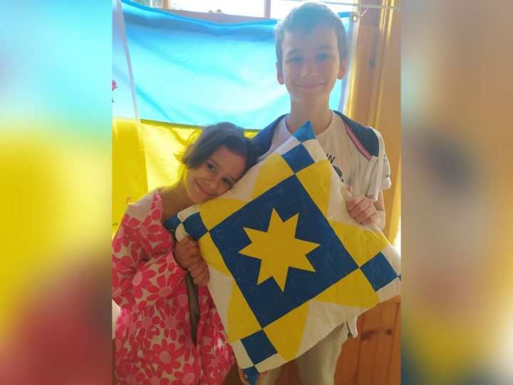Timur and Liana hold a patterned pillow with the Ukrainian colours, blue and yellow