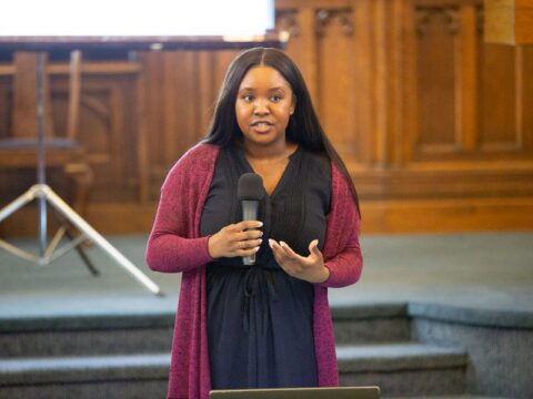 Jordana Wright speaks into a microphone inside the main congregating room of East End United Church