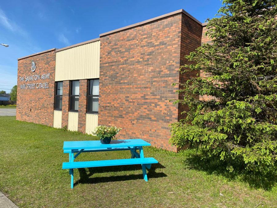 A rectangular brick building with a blue picnic table in the foreground