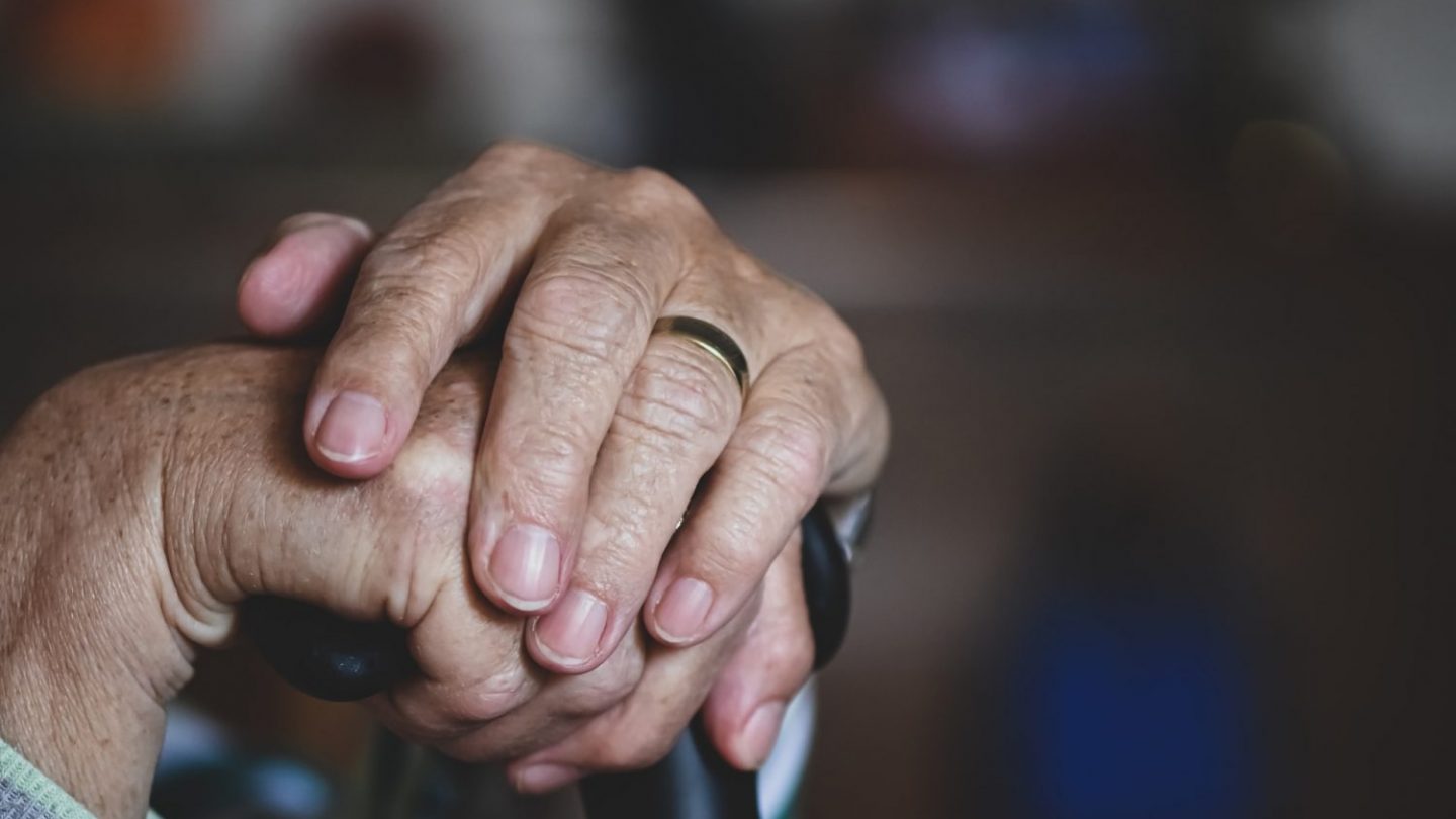 older person clasps hands on top of cane