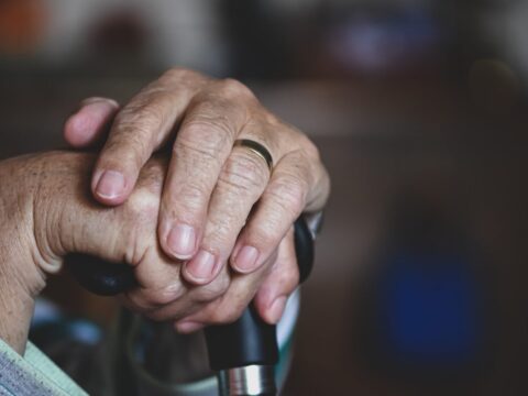 older person clasps hands on top of cane