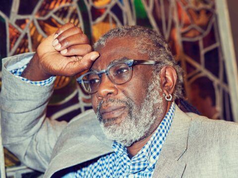 Michael Blair, the United Church's general secretary, a man with a grey beard and glasses, stares off into the distance while seated with a stained glass window behind him