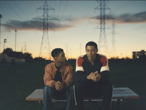 Two teenage boys sit on a picnic table in a park as the sun sets