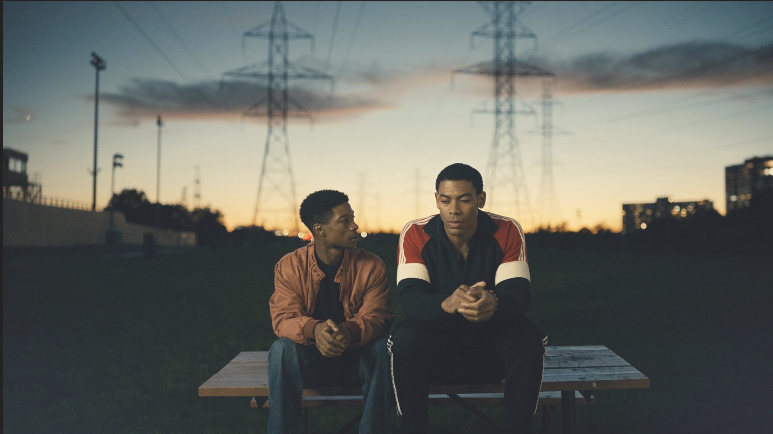 Two teenage boys sit on a picnic table in a park as the sun sets