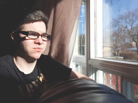 Young man with glasses looks out window