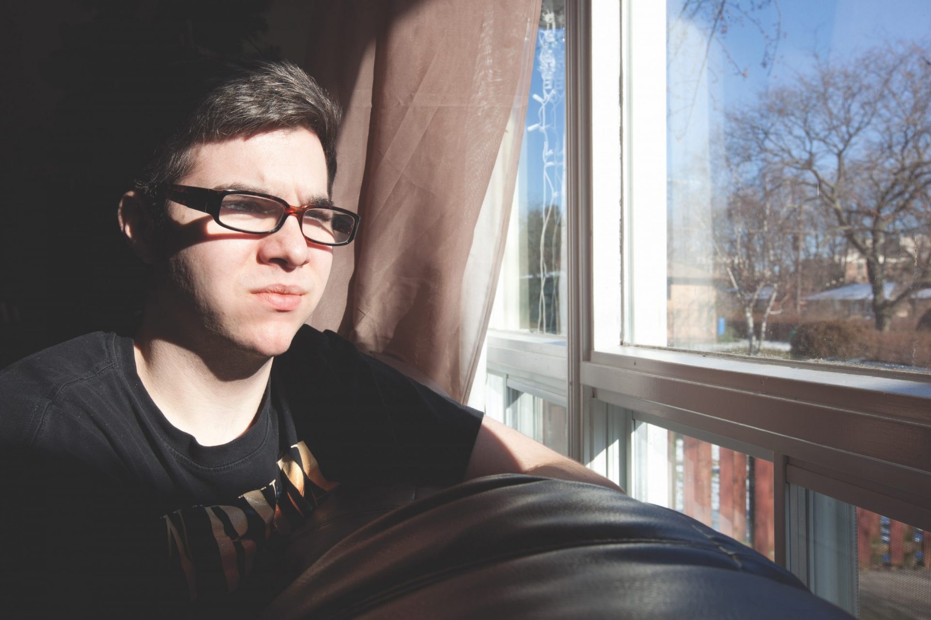 Young man with glasses looks out window