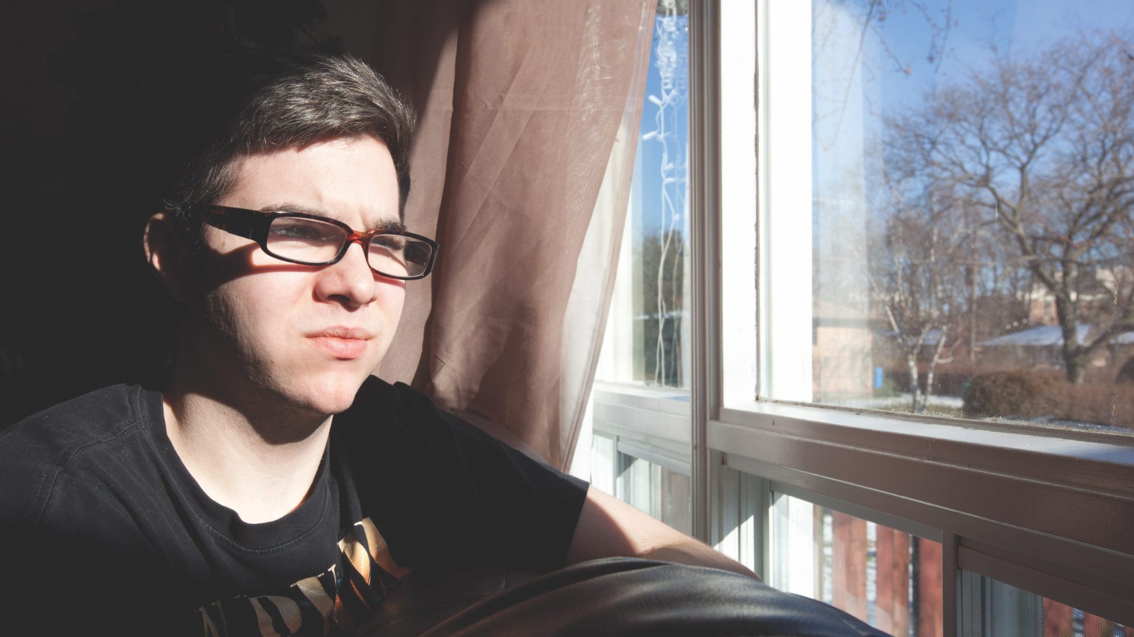 Young man with glasses looks out window