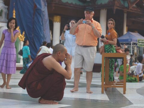 Tourists look at praying Buddhist monk in Burma