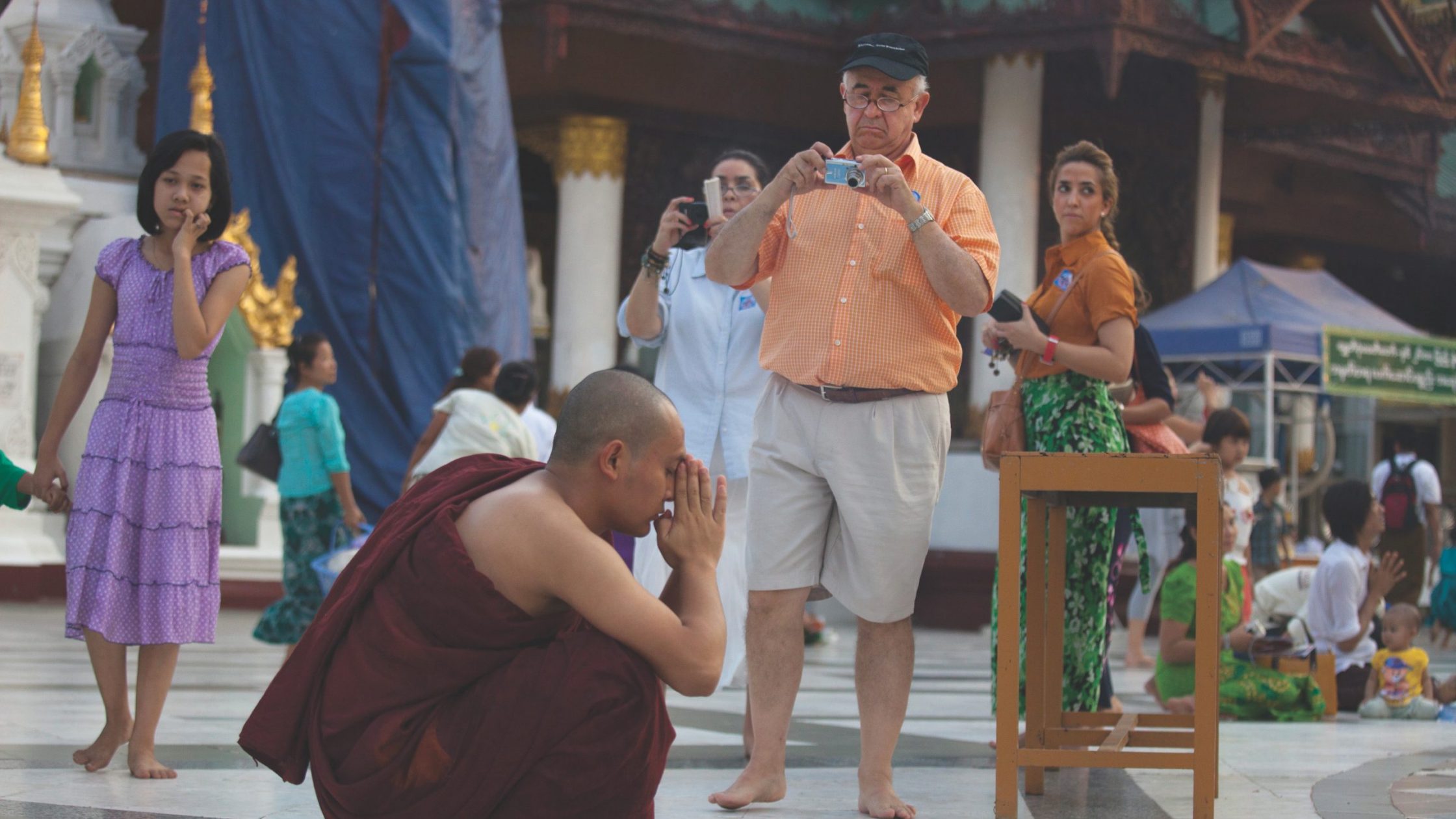 Tourists look at praying Buddhist monk in Burma
