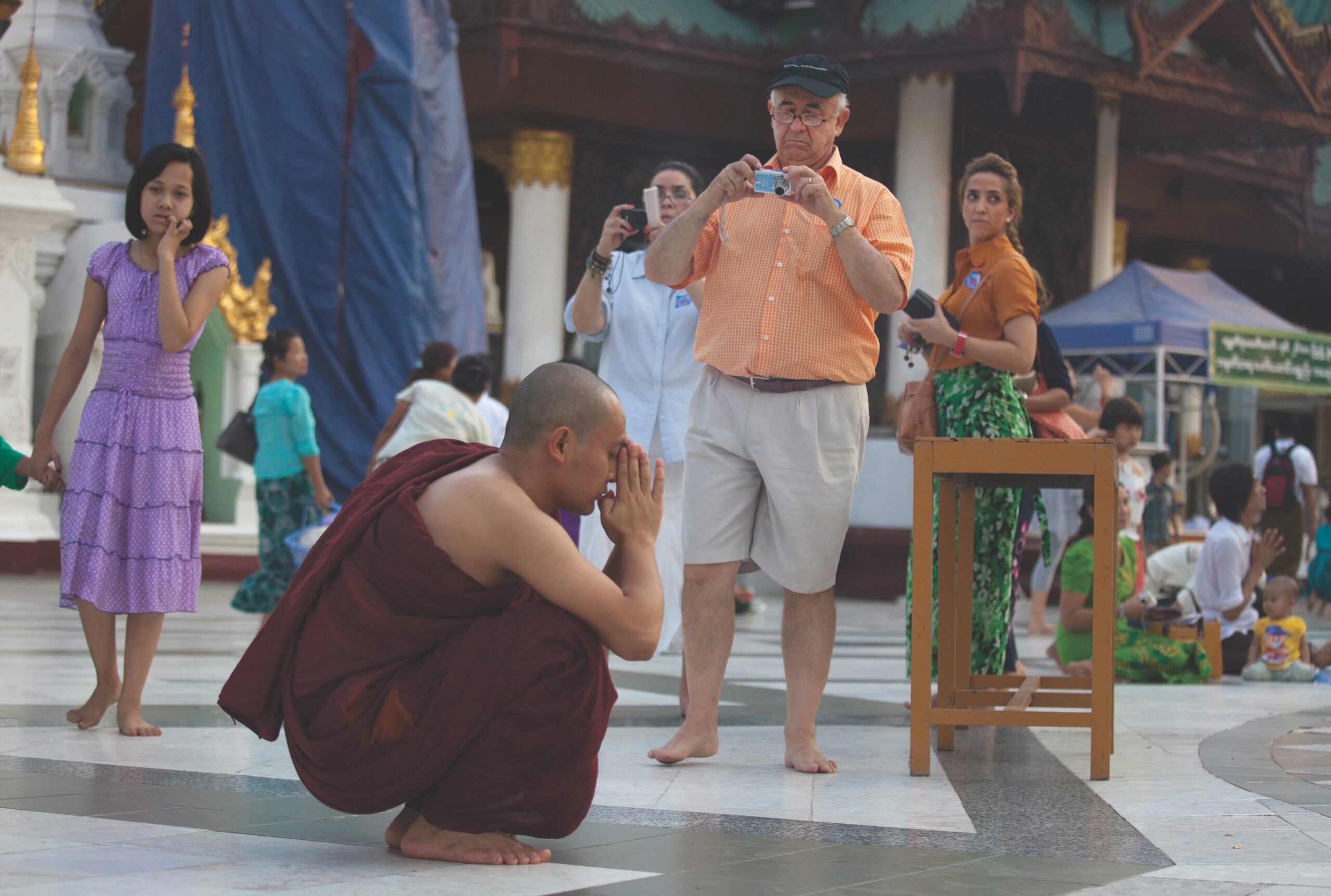 Tourists look at praying Buddhist monk in Burma