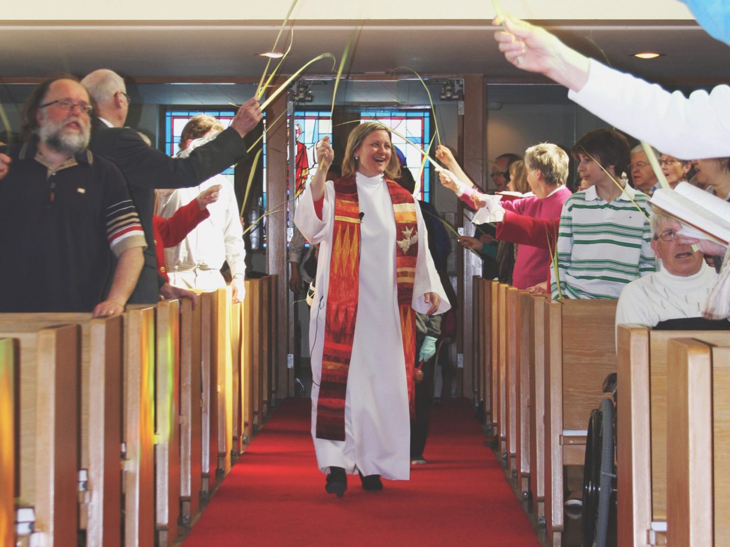 Clergy walks down church aisle under palm leaves