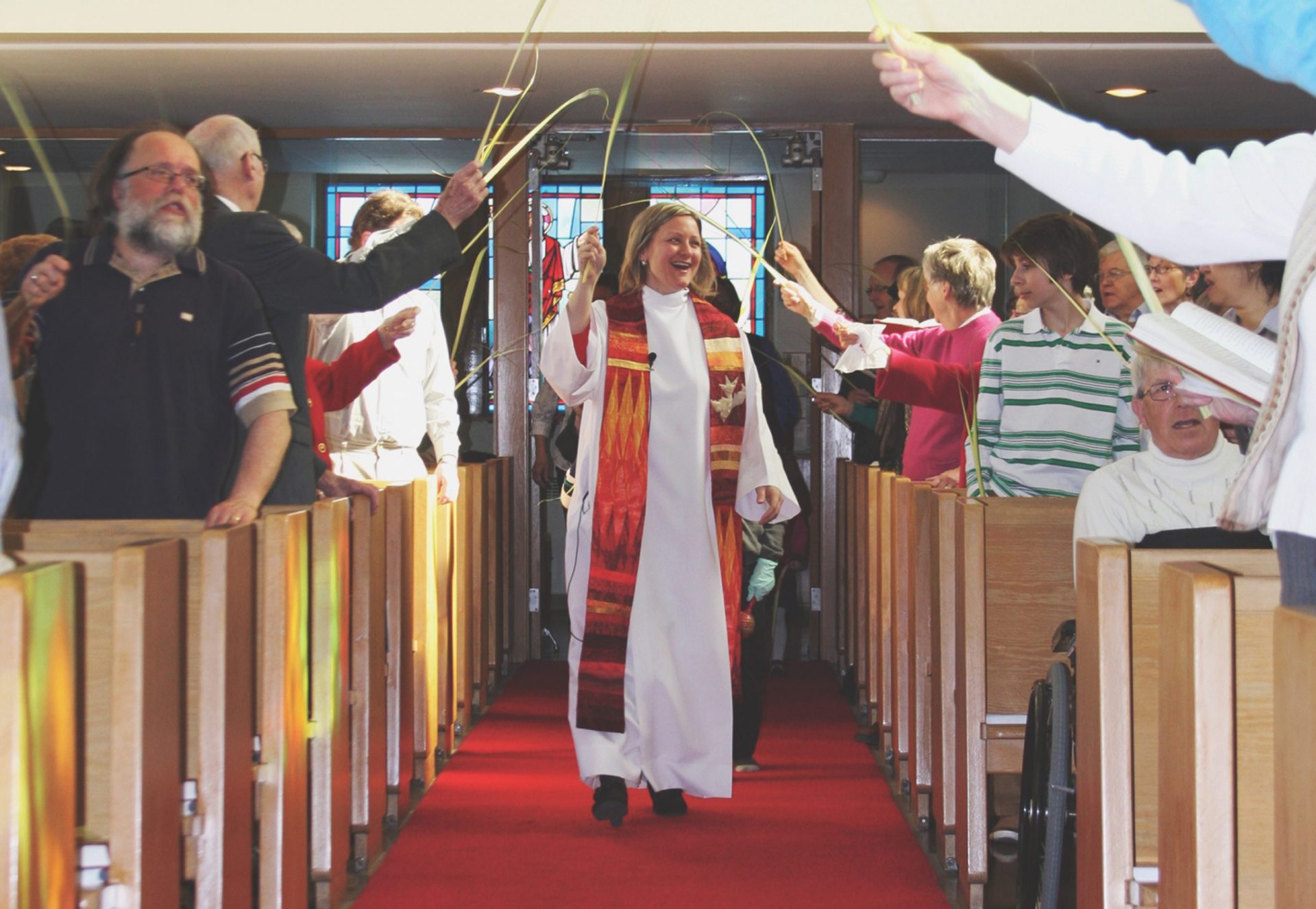 Clergy walks down church aisle under palm leaves
