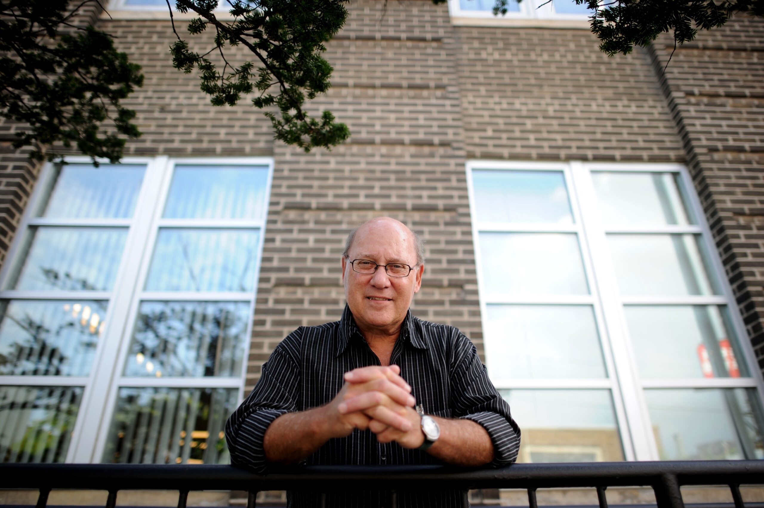 White man with clasped hands in front of building