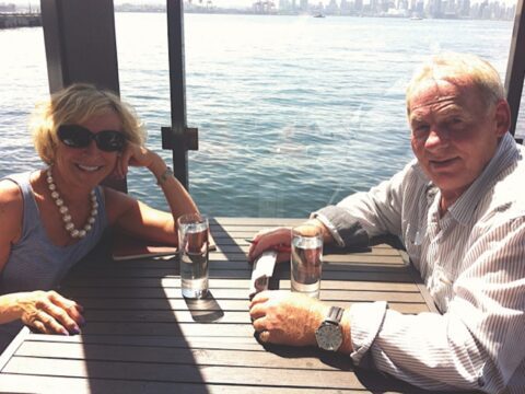 white-haired woman and man at table with ocean behind