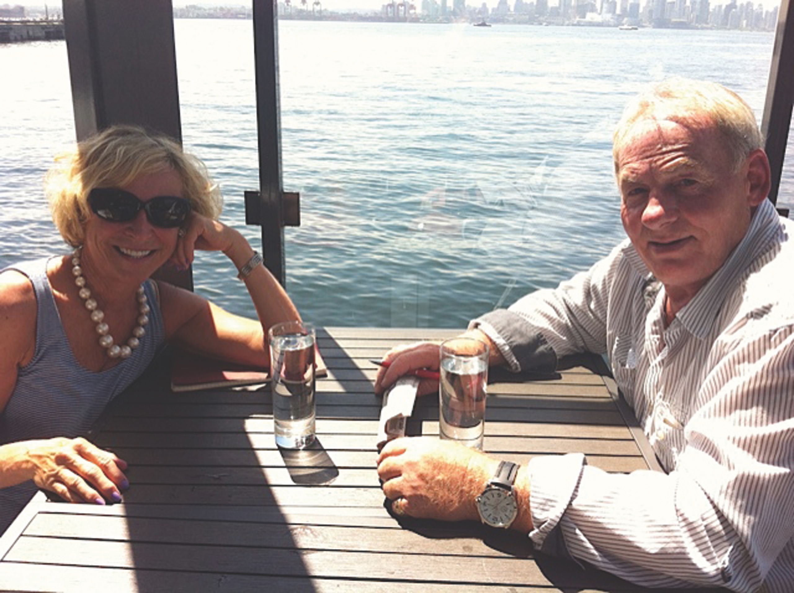 white-haired woman and man at table with ocean behind