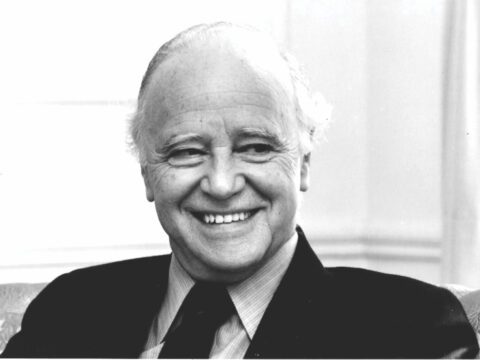 White man with white hair in dark suit smiling