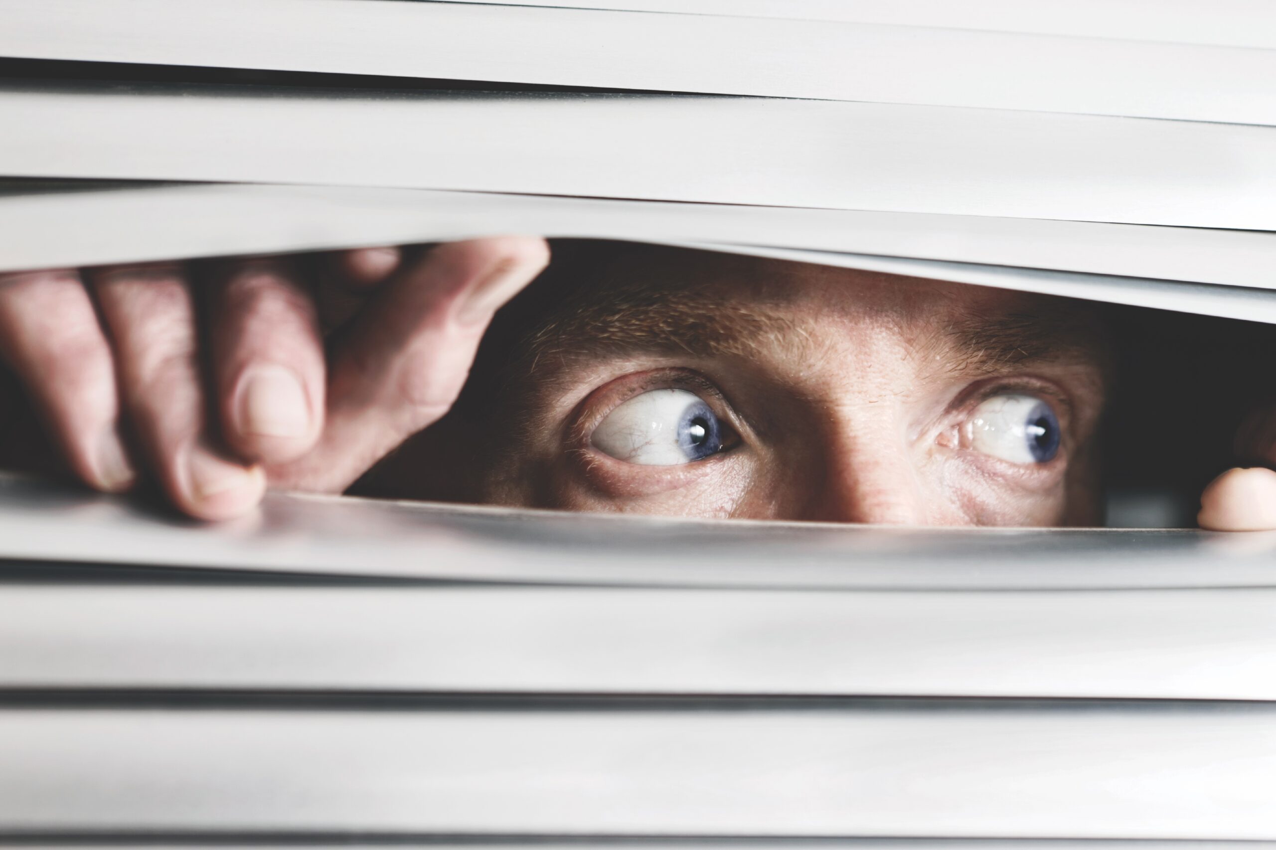 Person looking between slats of blind