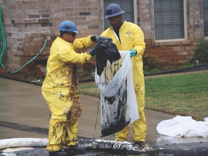 Men in hazmat suits put oil-soaked material in bags
