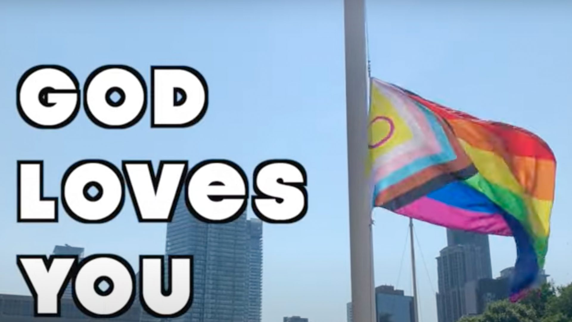 A pride flag flies in the background. White text next to it that says "God Loves You"