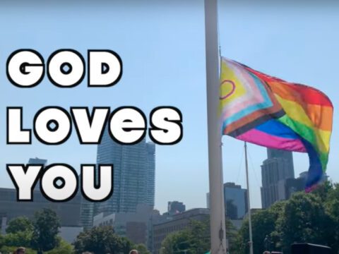 A pride flag flies in the background. White text next to it that says "God Loves You"