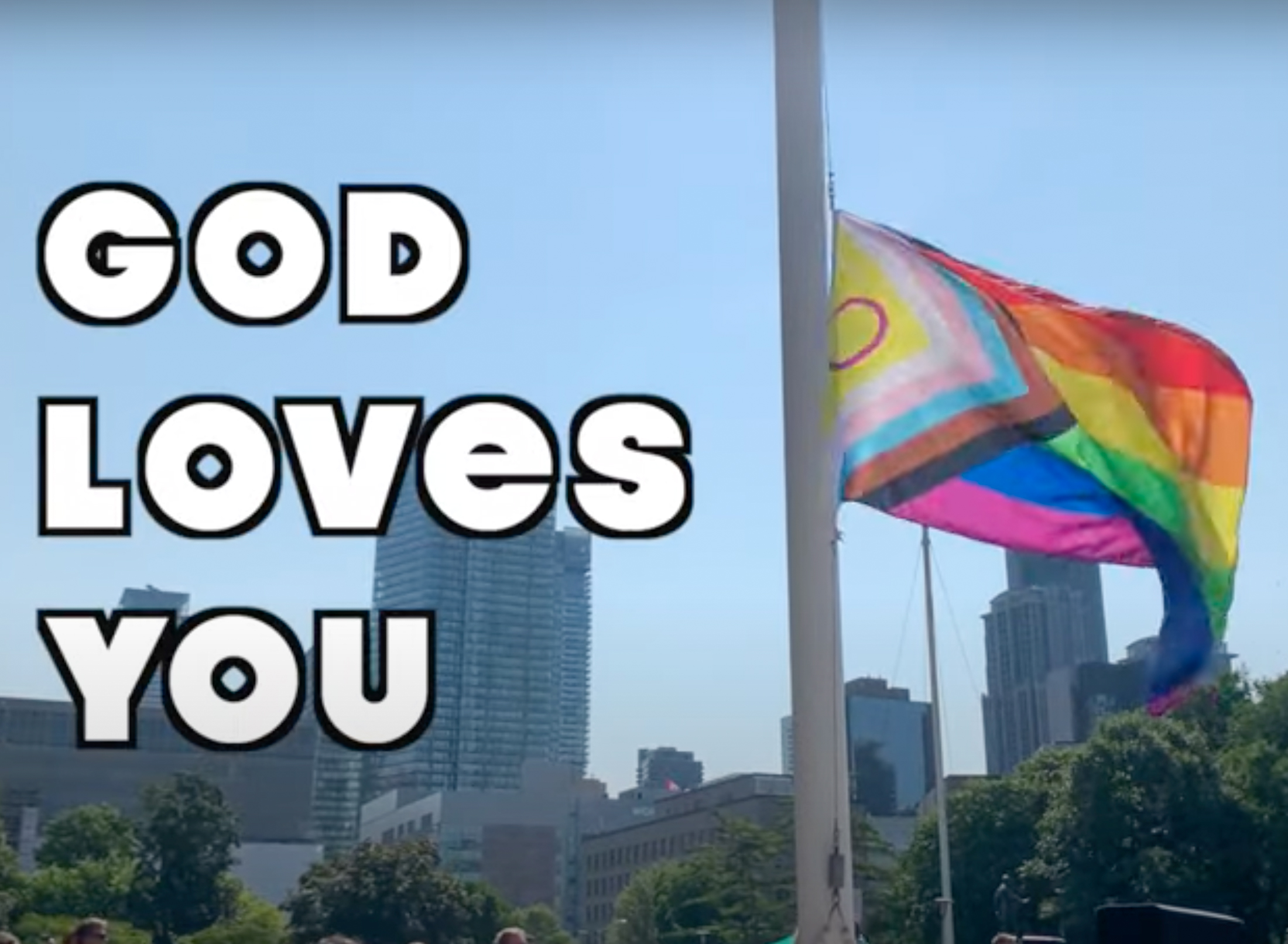 A pride flag flies in the background. White text next to it that says "God Loves You"