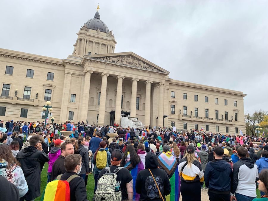 Anti-trans and homophobic counter-protest crowd with pride flags outside government building in Canada.