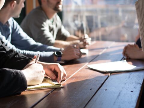 People sitting at a table with notebooks open and pens in their hands.
