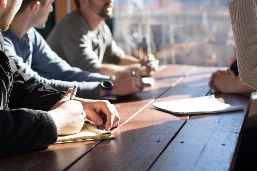 People sitting at a table with notebooks open and pens in their hands.