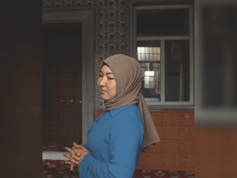 Woman dressed in a brown headscarf and a blue long sleeve blouse.