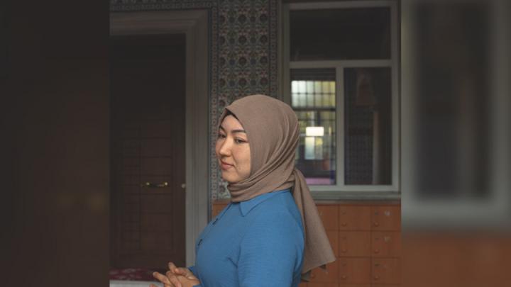 Woman dressed in a brown headscarf and a blue long sleeve blouse.