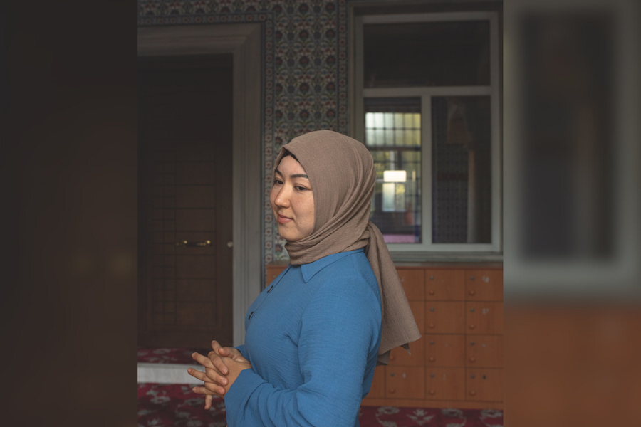 Woman dressed in a brown headscarf and a blue long sleeve blouse.