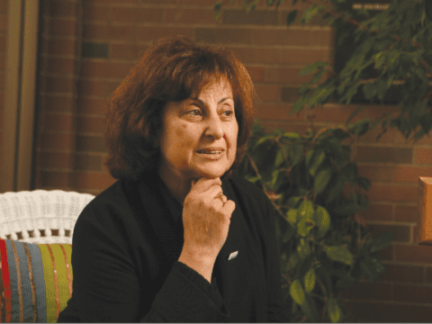 Dark-haired woman sits on white rattan sofa