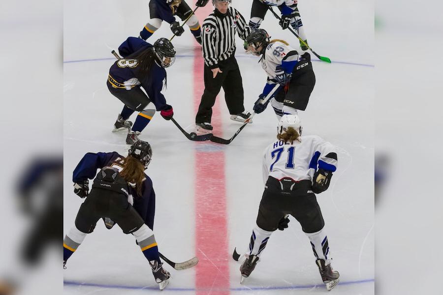 Women hockey players competing on ice with a referee in the middle.