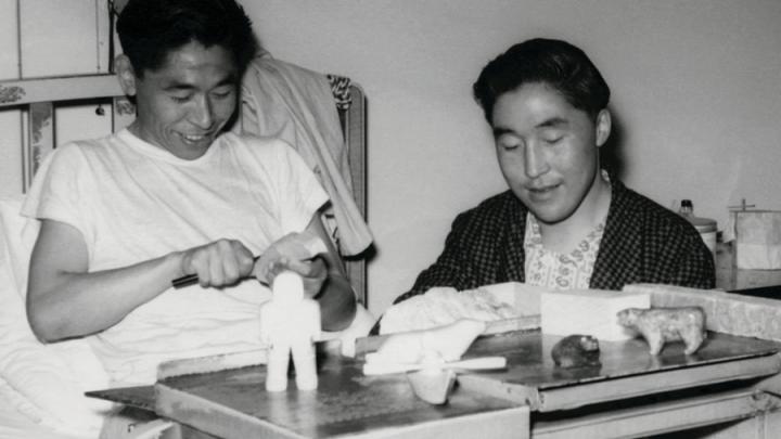 Black and white photo of Inuit men in hospital carving figures in soapstone