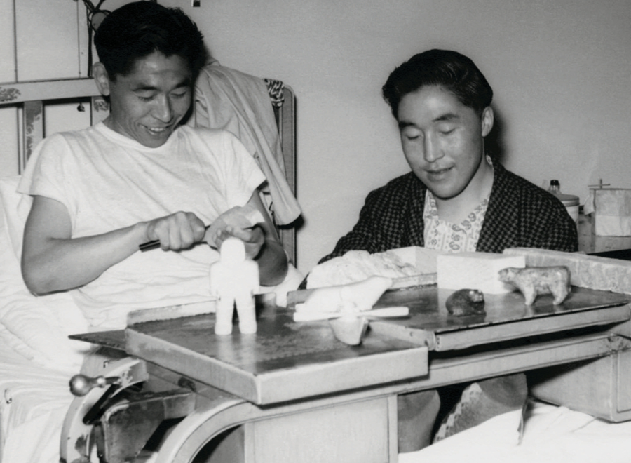 Black and white photo of Inuit men in hospital carving figures in soapstone
