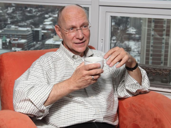 White man in shirt sitting in orange chair with cup of coffee