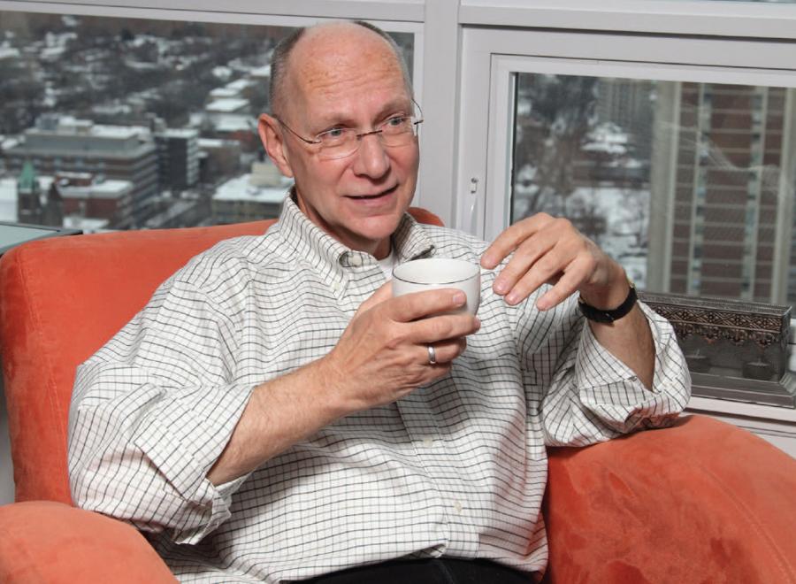White man in shirt sitting in orange chair with cup of coffee