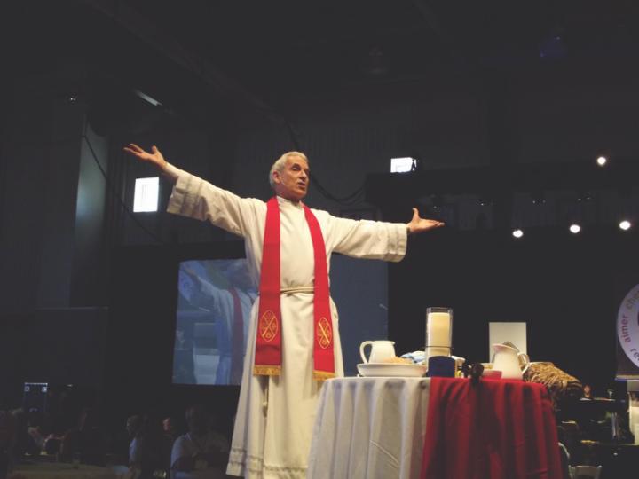 White man in clerical dress stands with open arms