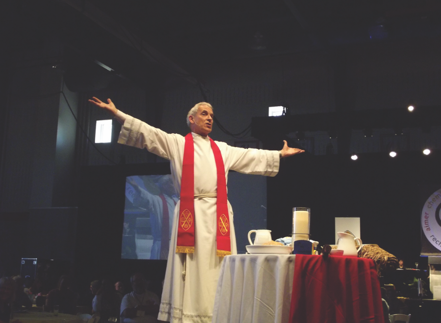 White man in clerical dress stands with open arms