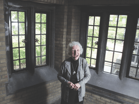 Older white woman standing in front of windows, smiling broadly