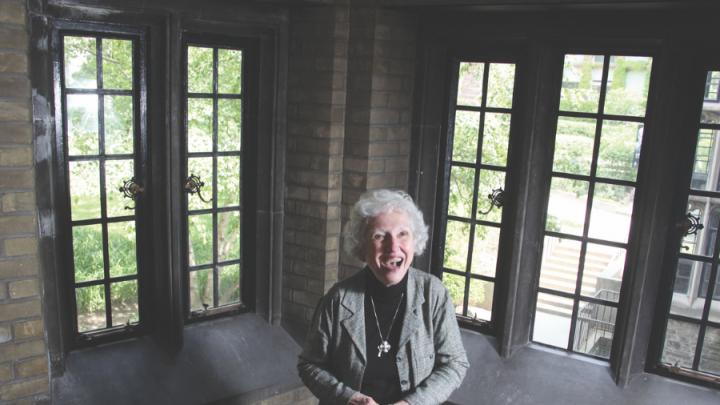 Older white woman standing in front of windows, smiling broadly