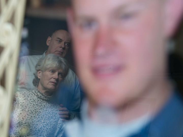 Older white couple in front of blurry large image of young man