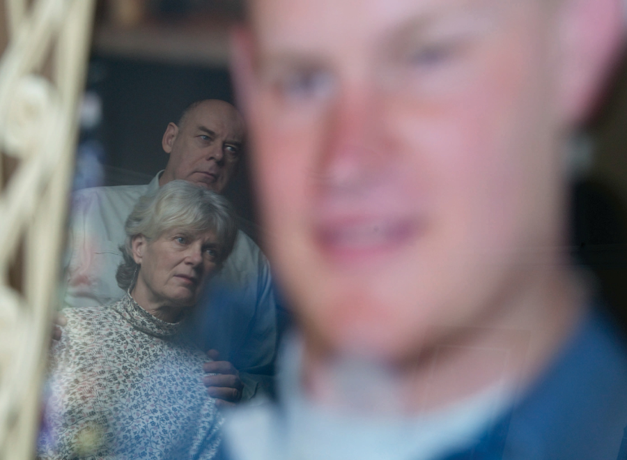 Older white couple in front of blurry large image of young man