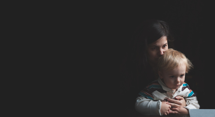 Black background and a woman with black hair holding a baby with blond hair in a striped shirt.