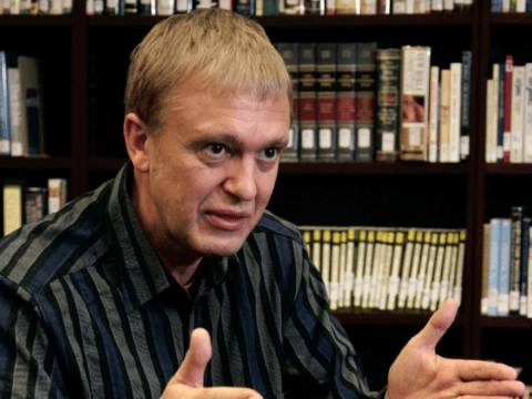 White man sitting in front of shelves of books