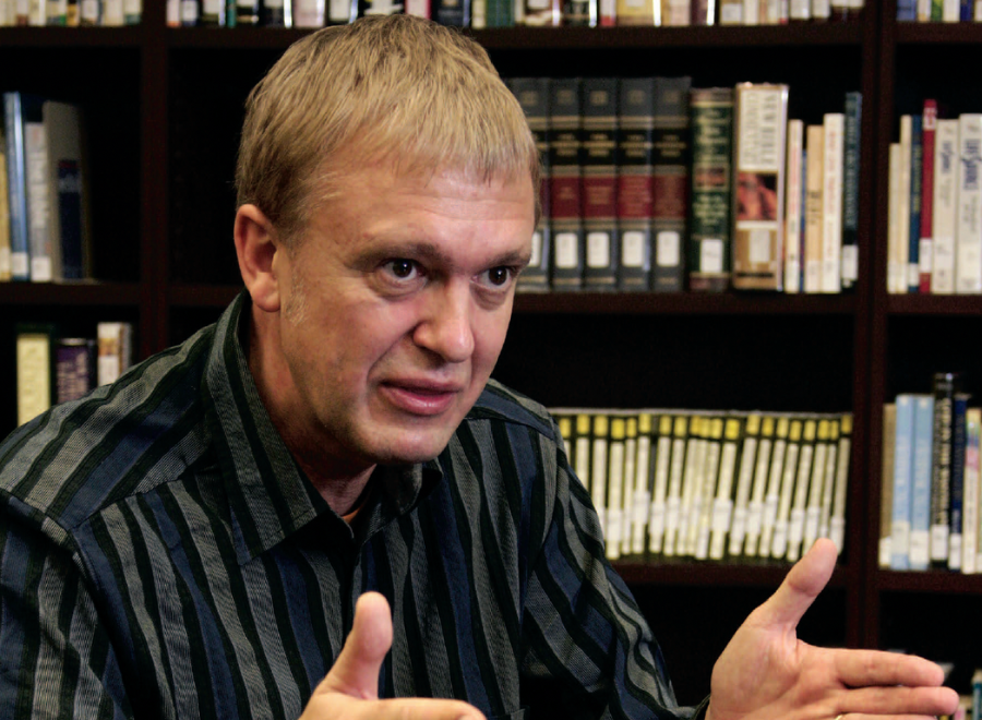 White man sitting in front of shelves of books