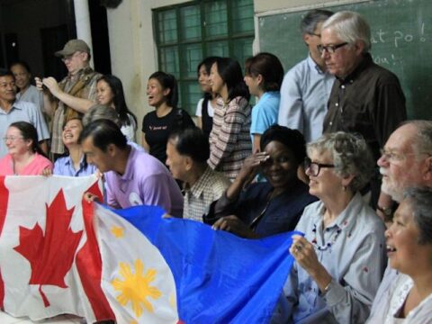 Two rows of people standing and kneeling together. The people kneeling are holding a Canadian flag and a Philippines flag.
