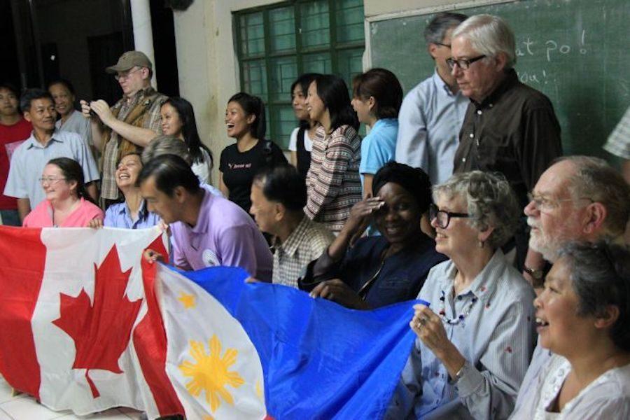 Two rows of people standing and kneeling together. The people kneeling are holding a Canadian flag and a Philippines flag.